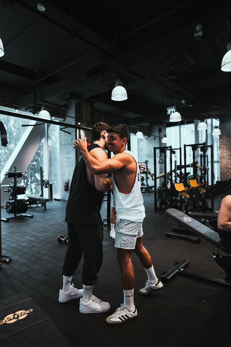 Two people training side by side in a gym, each carrying a weighted bag on their shoulders.